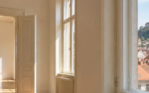 Leere Altbauwohnung mit Fischgrätparkett, Blick über Grazer Dächer zum Schlossberg mit Uhrturm